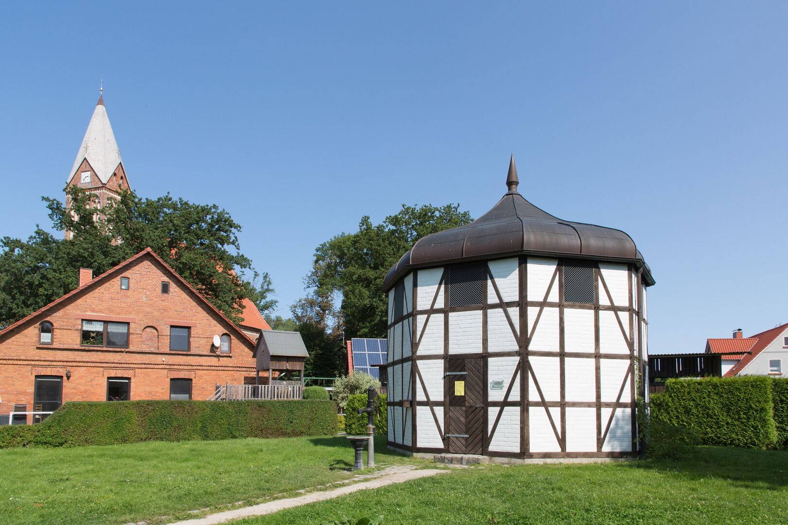 Achteckiges Häuschen Fachwerk weiß vermauert, im Hintergrund die Kirche