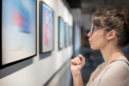 eine Frau mit Brille schaut sich bilder in einer Galerie an ener wand an