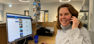 Frau am Telefon sitzt vor ihrem Computer am Empfang und lächelt in die Kamera